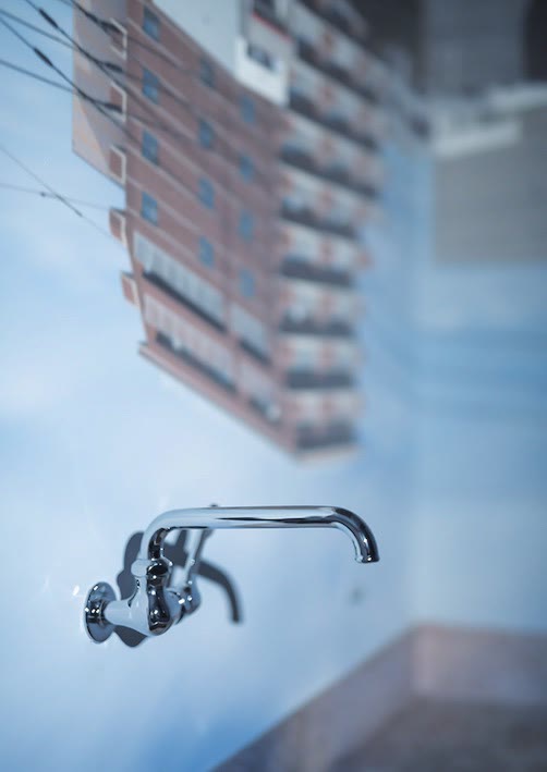 Un grifo en la pared con un edificio de viviendas y el cielo proyectados al revés sobre él