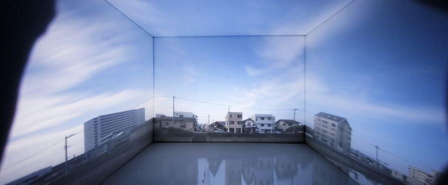 部屋の壁と床いっぱいに、空と建物の風景が横長に映り込んでいる