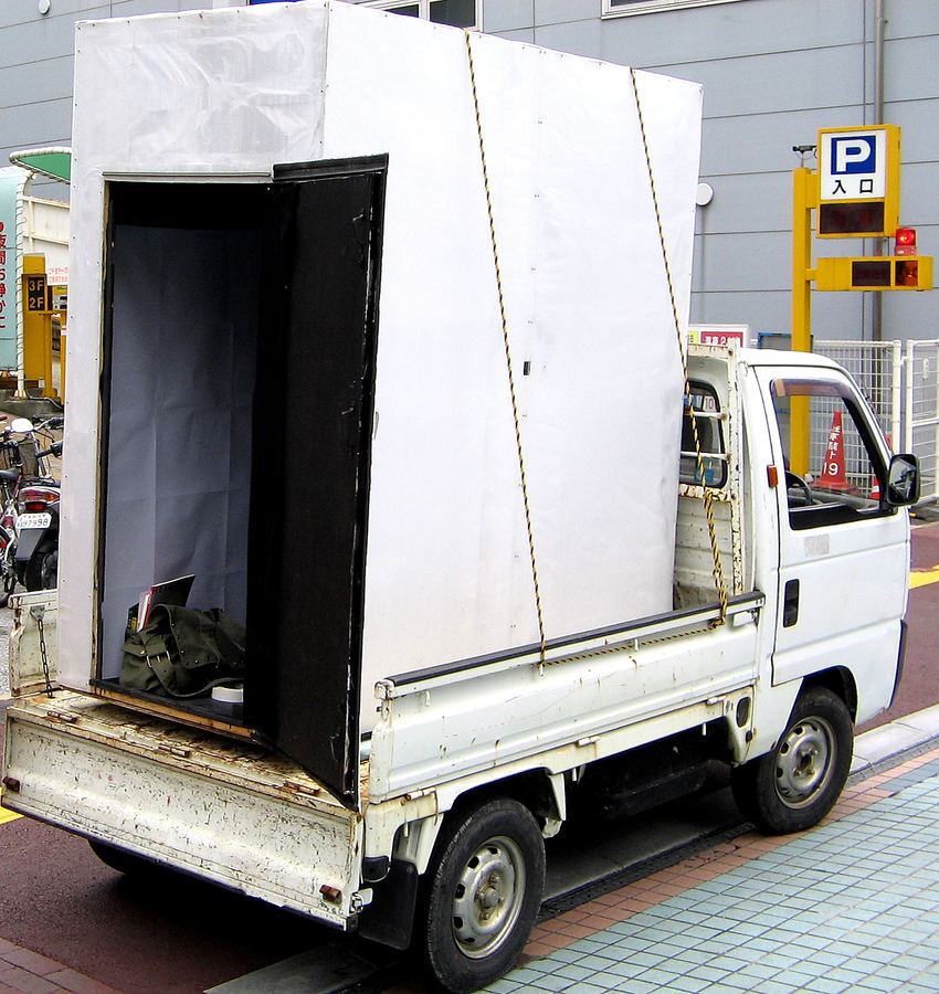 軽トラックの荷台に載せた、人が入れる大きさの白い箱型カメラ。側面の扉が開いている