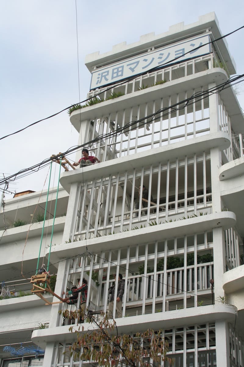 El edificio con su rótulo “Sawada Mansion” y el bastidor de madera suspendido con cuerdas