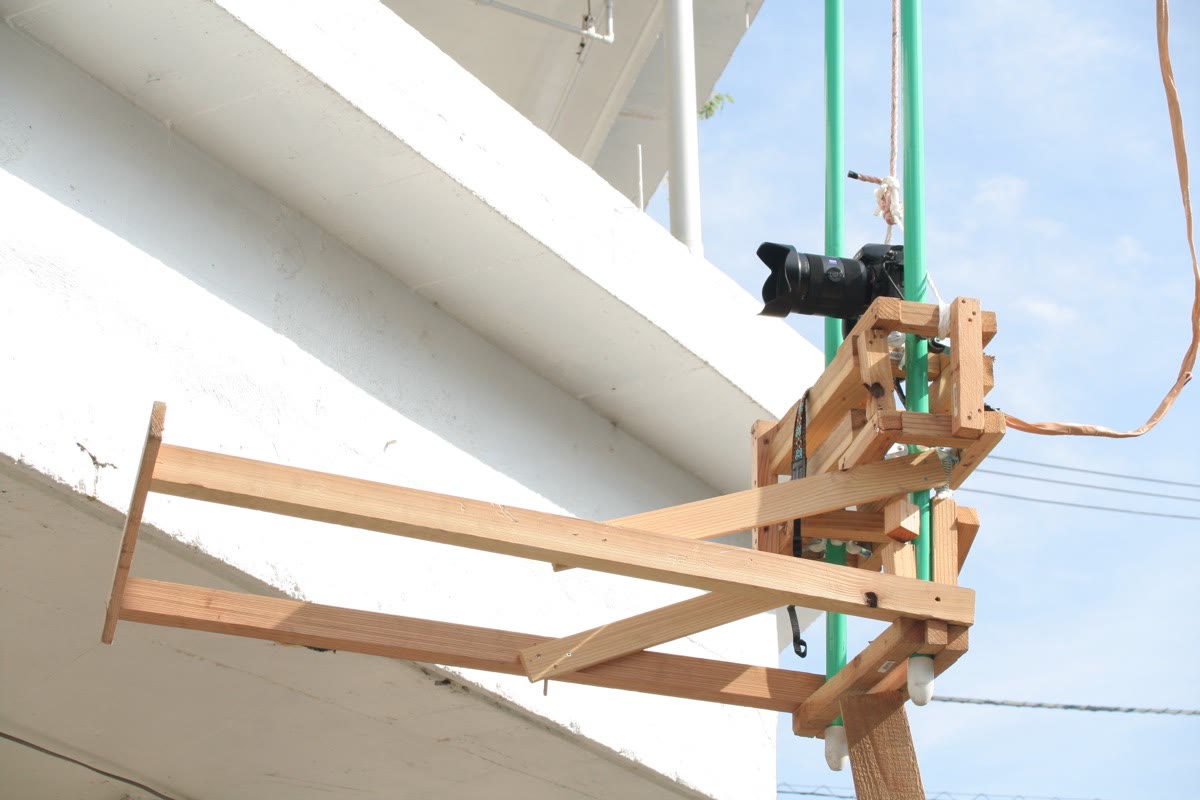 El bastidor escáner —una cámara montada en un brazo de madera— suspendido con cuerdas verdes junto al edificio